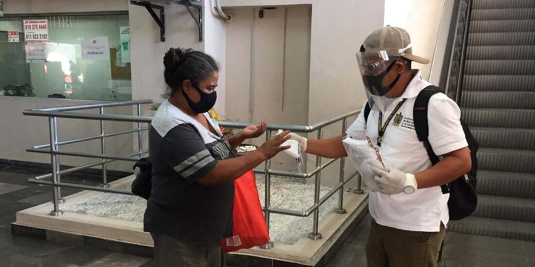 Pasajera recibe un cubrebocas después de colocarse gel antibacterial en las manos.