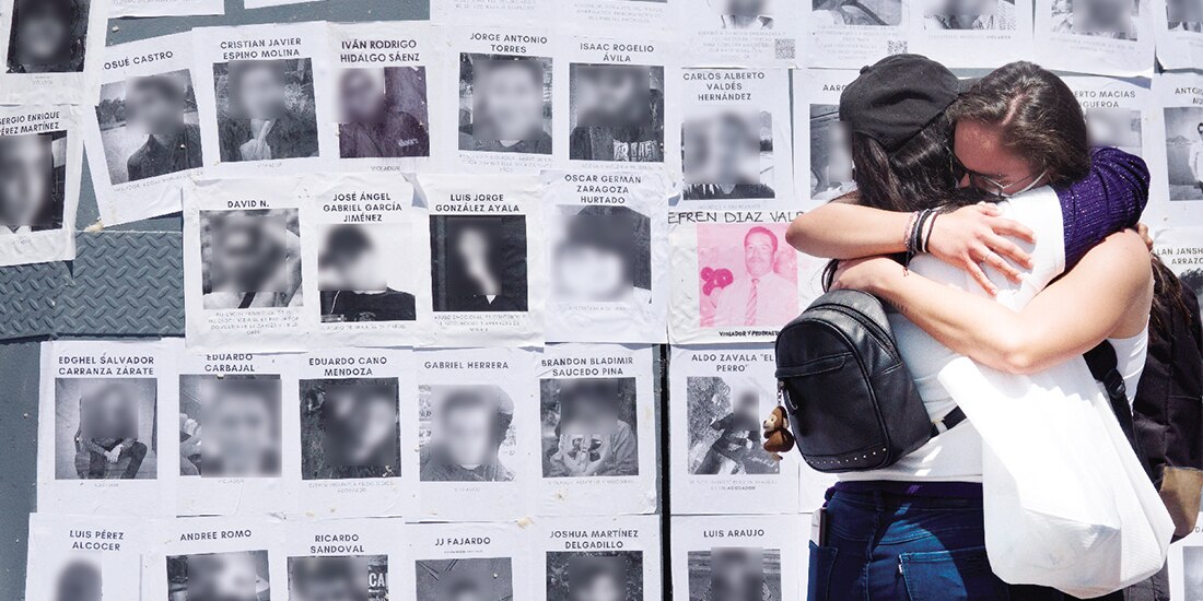 Dos jóvenes lloran frente a un tendedero con fotos de presuntos agresores de mujeres, en 2022.