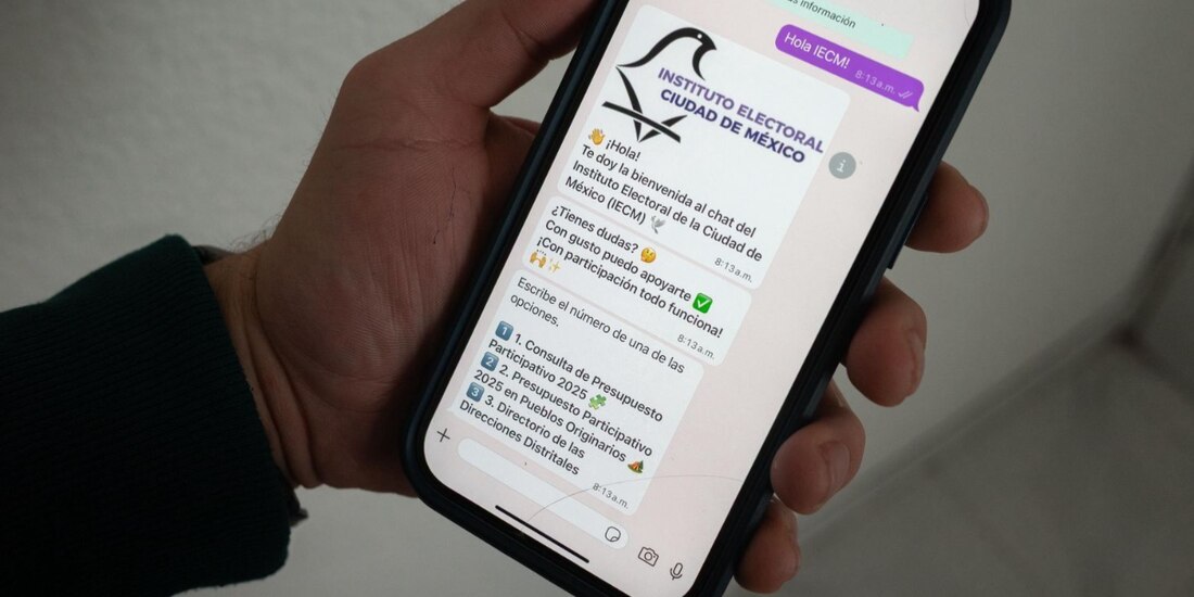 Una persona sostiene un celular con una plática con el chatbot del IECM.