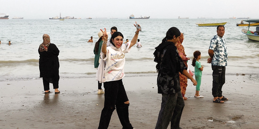 Gente camina por la playa con barcos en Ormuz, en Irán, el 22 de mayo