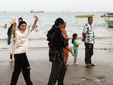Gente camina por la playa con barcos en Ormuz, en Irán, el 22 de mayo