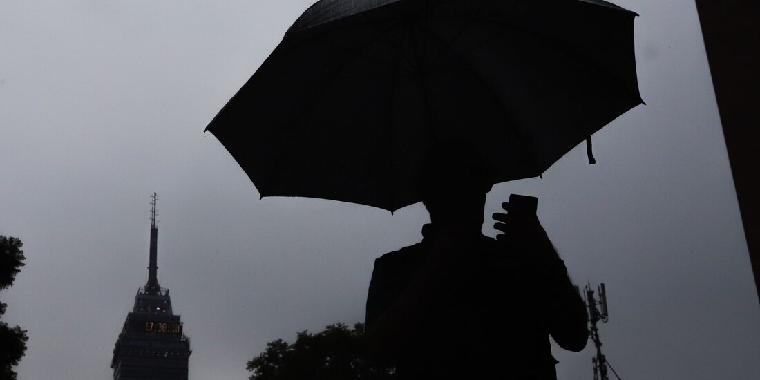 Una persona observa su celular mientras camina utilizando un paraguas para protegerse de la lluvia.