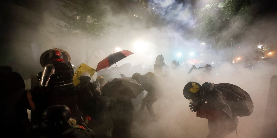 Manifestantes se cubren con sombrillas del gas lacrimógeno, en Portland.