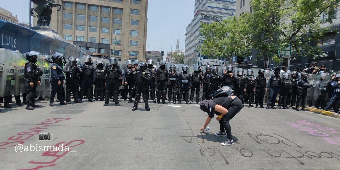 Una feminista realiza una pinta en el piso frente a policías capitalinos equipados con escudos antimotines.