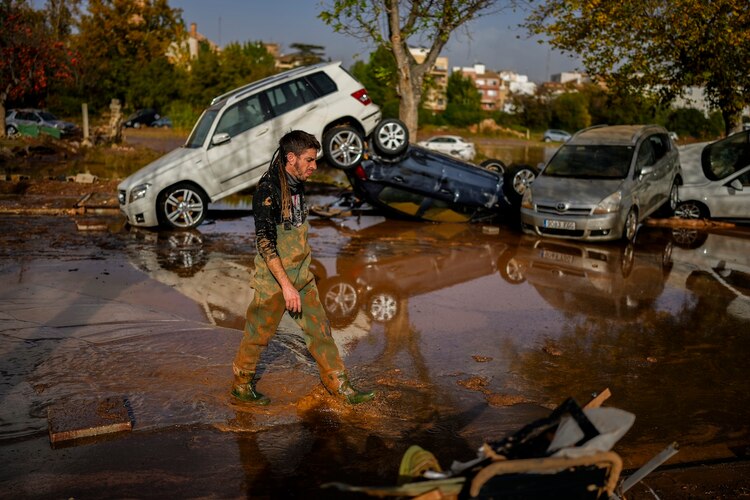 Un ciudadano camina frente a una pila de autos arrastrados por el fuerte nivel de lluvia e inundaciones.