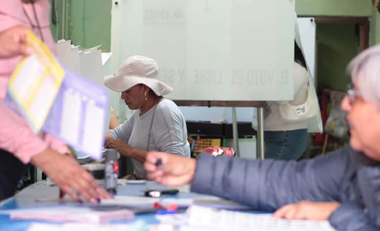 Dos personas sufragan en Iztacalco mientras arriba un hombre a la casilla.