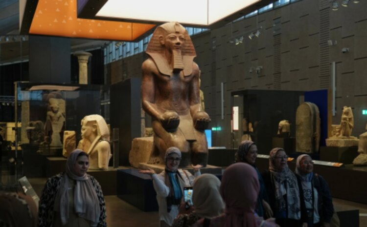 Visitantes posan para una foto grupal bajo la estatua de Hatshepsut, en el Gran Museo Egipcio en Giza, Egipto, el viernes 23 de mayo de 2025.