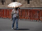 Tercera ola de calor continúa en México; en foto, una mujer se cubre del sol mientras camina por el Zócalo de la Ciudad de México.