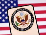 El logo del Departamento de Estado; al fondo, la bandera de Estados Unidos.