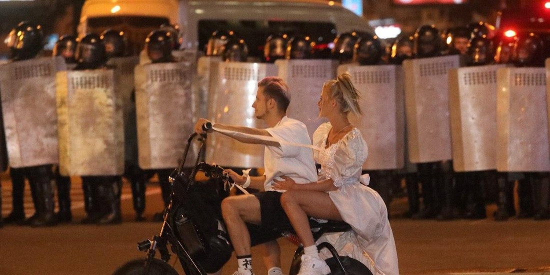 Una chica con vestido de novia pasa en una motoneta con su novio frente a un bloque de policías durante una manifestación en Minsk